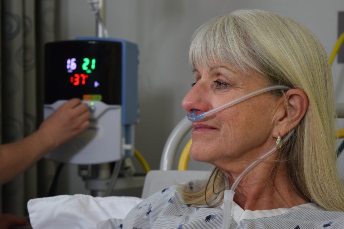 Image of a patient. A Vapotherm Precision Flow unit is visible in the background.