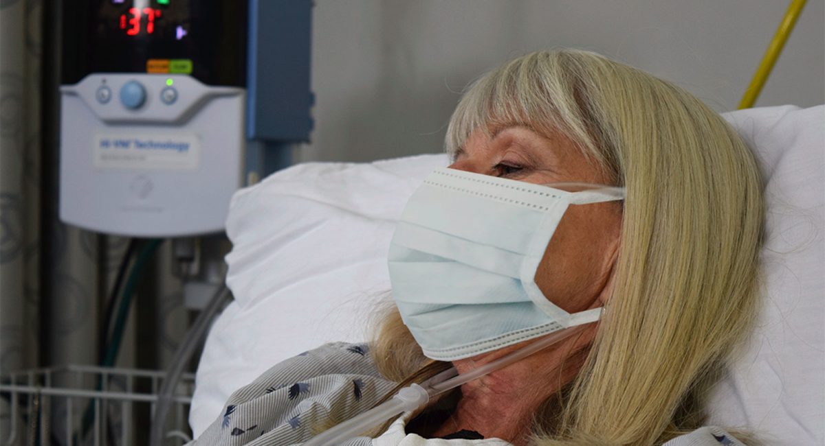 Image of a female patient sleeping with a surgical mask. A Vapotherm Precision Flow unit is visible next to the bed.