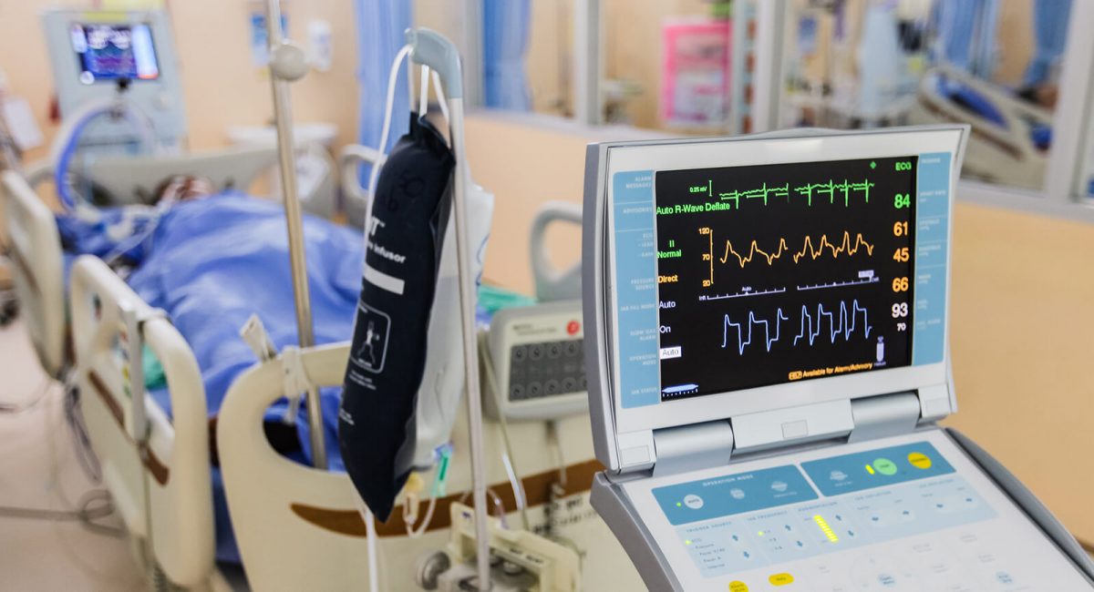 Image of a hospital room with a patient in the distance and a vitals monitor in the front