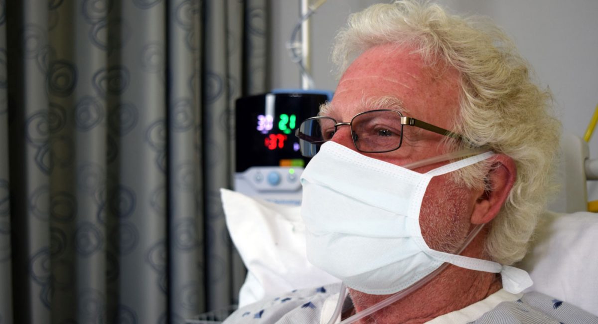 Image of a male patient wearing a surgical mask. A Vapotherm Precision Flow unit is visible in the background.