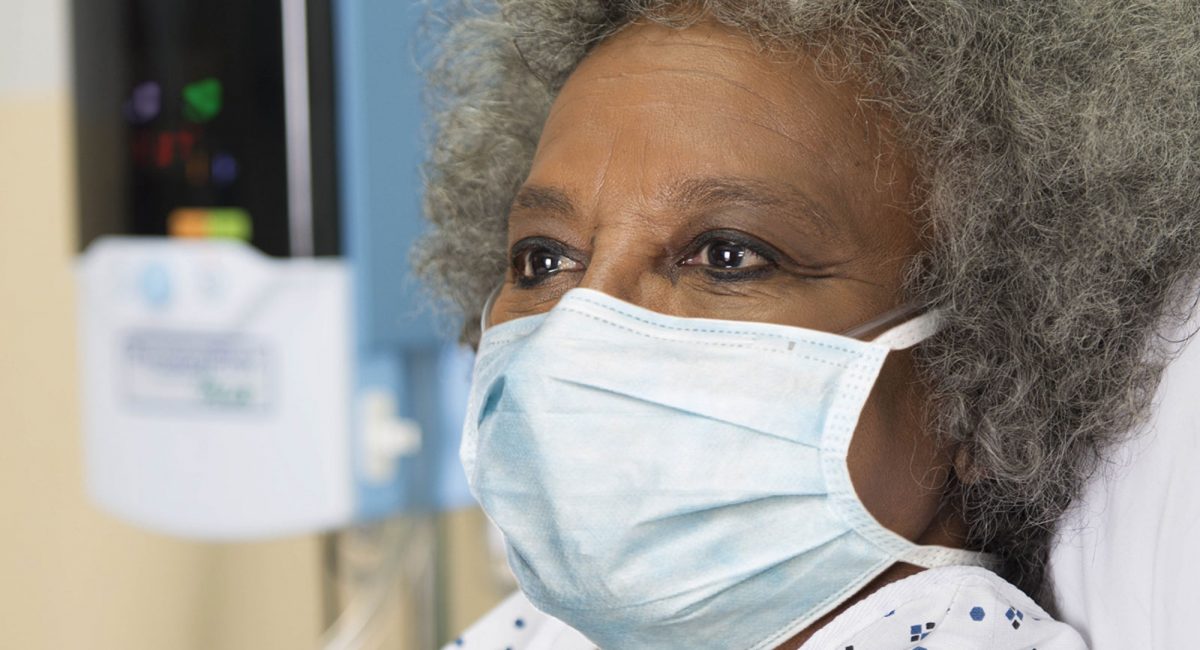 Image of a patient with a surgical mask. A Vapotherm Precision Flow unit is visible in the background.