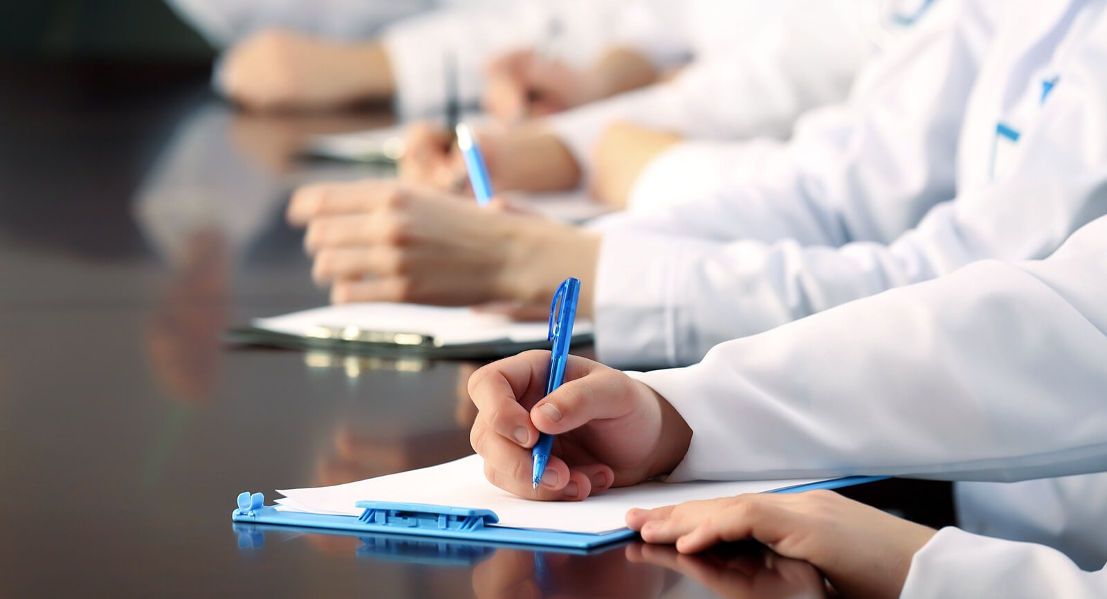 image of a row of lab coat wearing people writing on clip boards